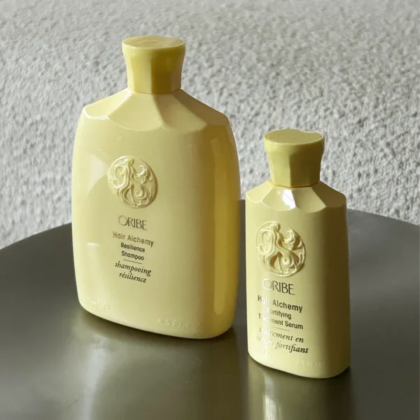 Oribe Hair Alchemy Resilience produkter, herunder shampoo, conditioner og et serum, arrangeret på en metal skammel